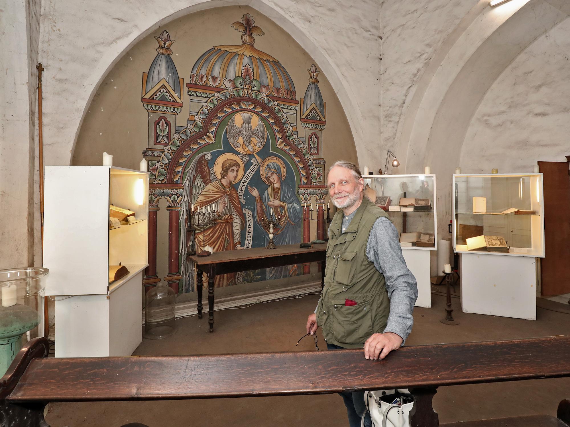 Kirchenvorstand Jürgen Schram in der Hasenaeckerschen Bibliothek in St. Josef. Das Wandbild zeigt Mariä Verkündigung.